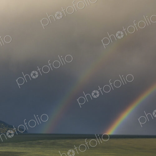 A double rainbow in a dark stormy sky, reaching down to the horizon.