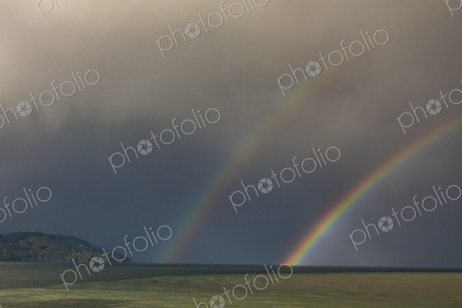 A double rainbow in a dark stormy sky, reaching down to the horizon.