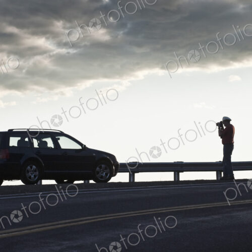 A driver stops to take a photograph at sunset on a road trip. A driver stops to take a photograph at sunset on a road trip.