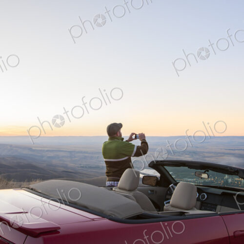 A driver stops to take a photograph at sunset , road trip with his convertible sports car.