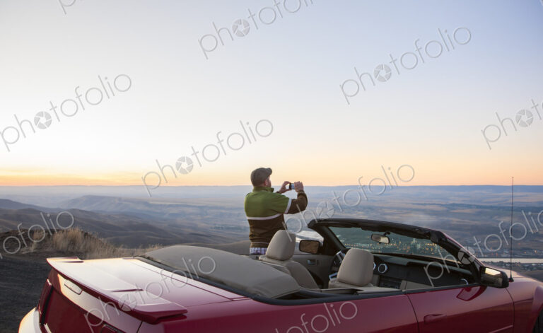 A driver stops to take a photograph at sunset , road trip with his convertible sports car.