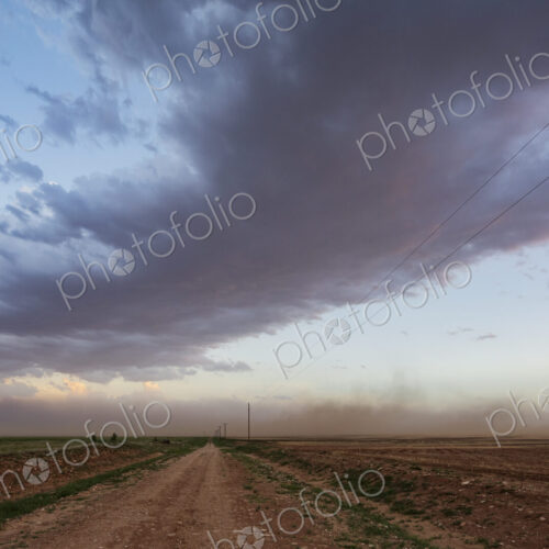 A dust storm approaching along a road at dusk. A dust storm approaching along a road at dusk.