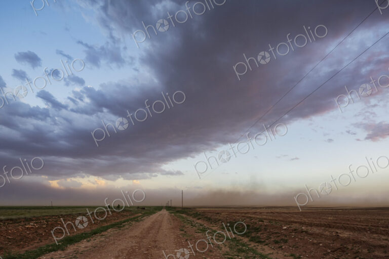 A dust storm approaching along a road at dusk.