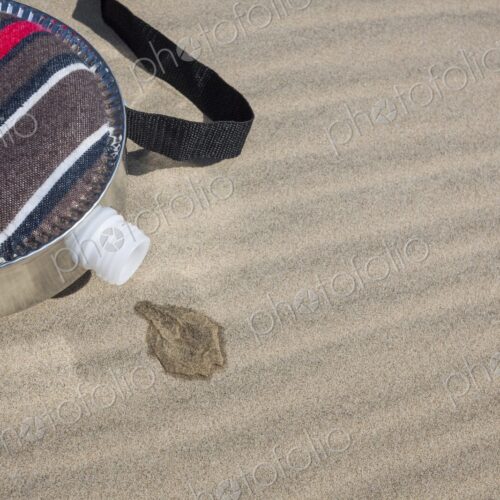 A fabric-covered canteen rests on rippled sand dunes with a small puddle of spilled… A fabric-covered canteen rests on rippled sand dunes with a small puddle of spilled…
