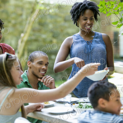 A family gathering, men women and children around a table in a garden in summer.
