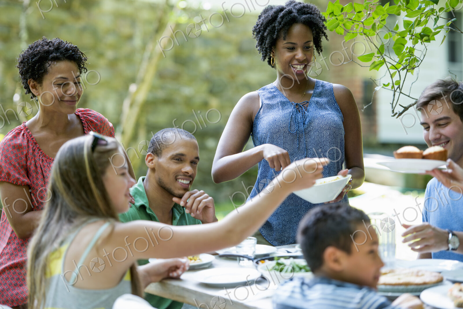 A family gathering, men women and children around a table in a garden in summer.