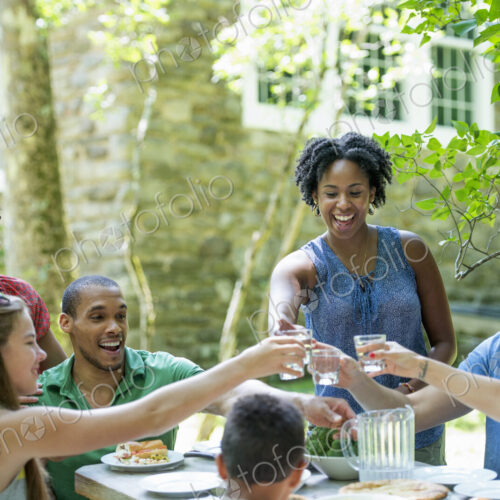 A family gathering, men women and children around a table in a garden in summer.