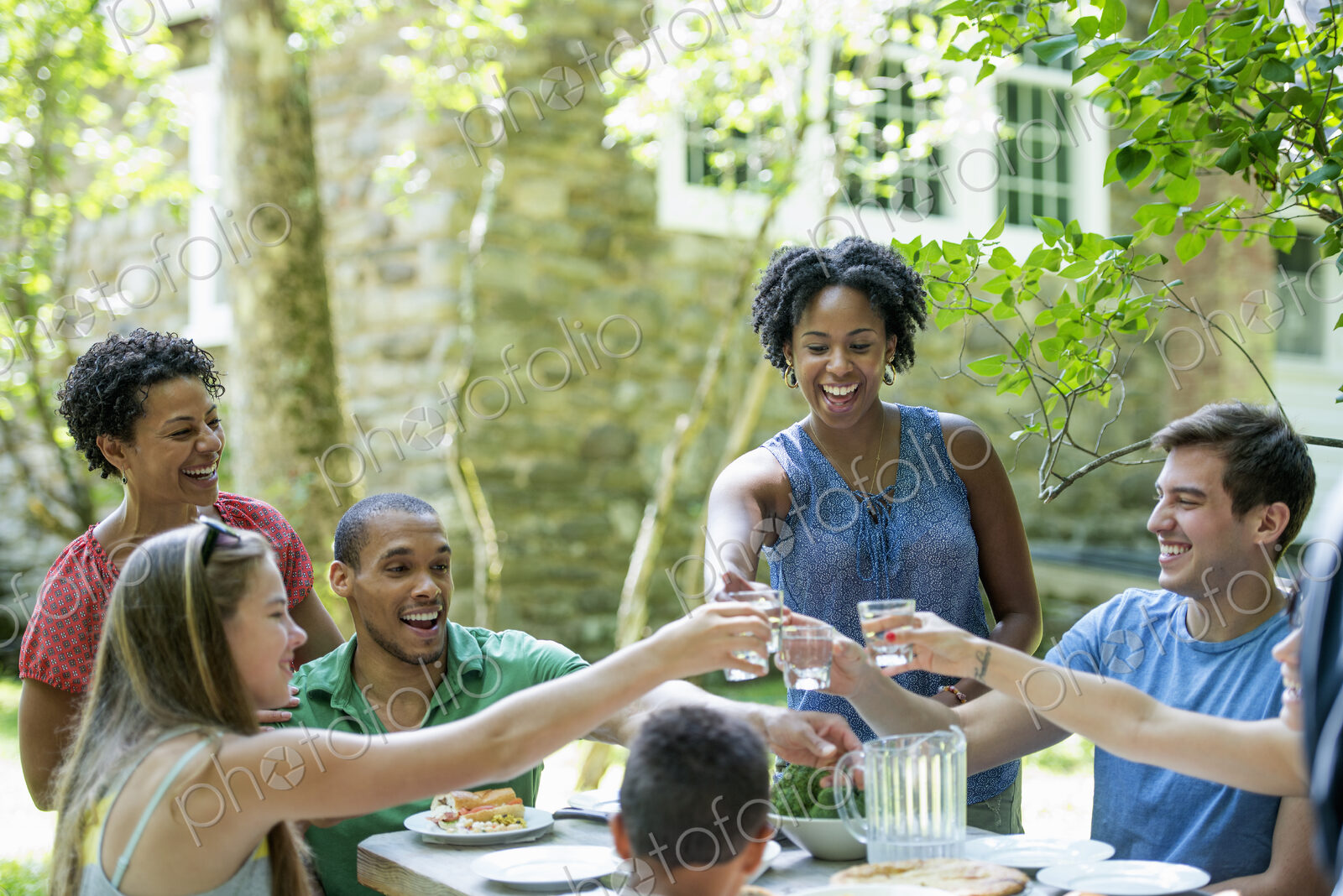 A family gathering, men women and children around a table in a garden in summer.