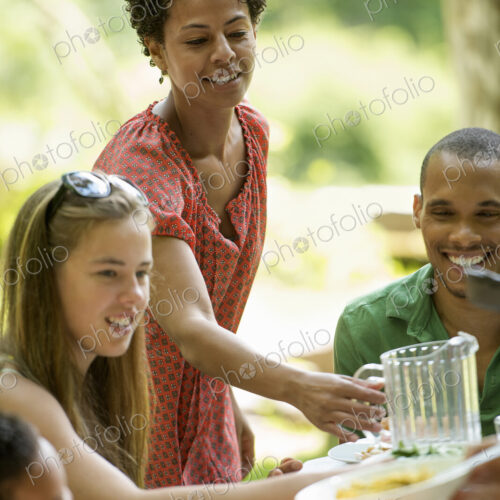 A family gathering, men women and children around a table in a garden in summer.