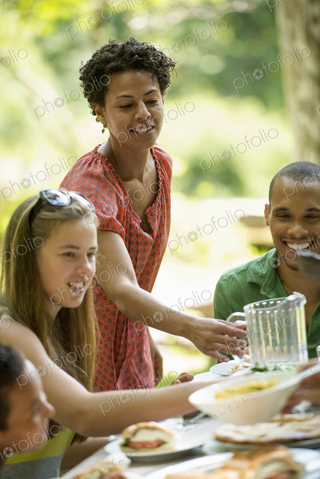 A family gathering, men women and children around a table in a garden in summer.