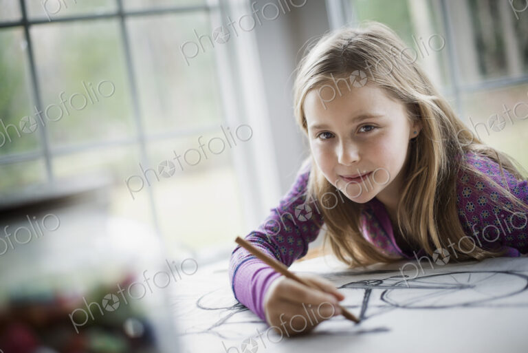 A family home. A child sitting at a table using a pencil and creating a line drawing.…