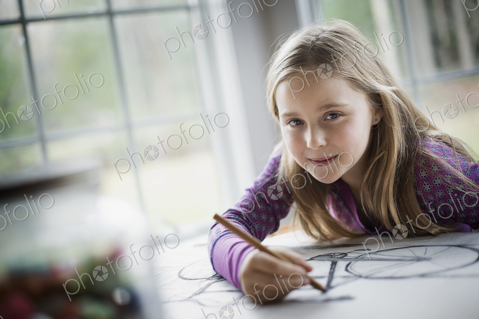 A family home. A child sitting at a table using a pencil and creating a line drawing.…