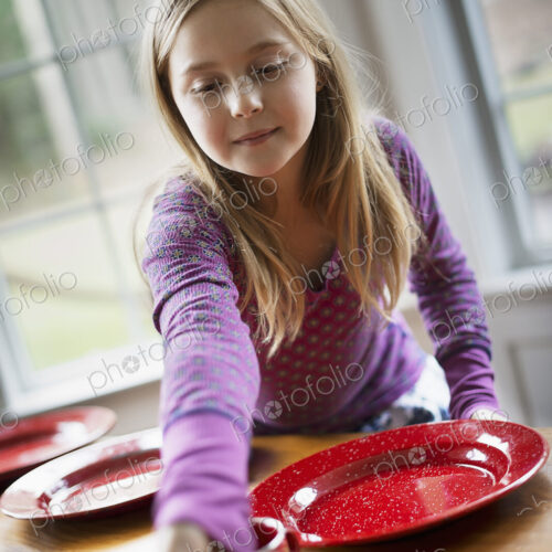 A family home. A young girl laying the table with plates and bowls for a meal. A family home. A young girl laying the table with plates and bowls for a meal.