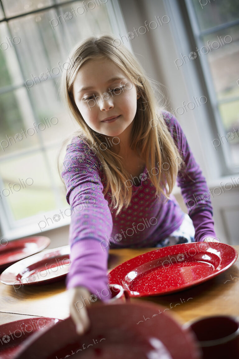 A family home. A young girl laying the table with plates and bowls for a meal.