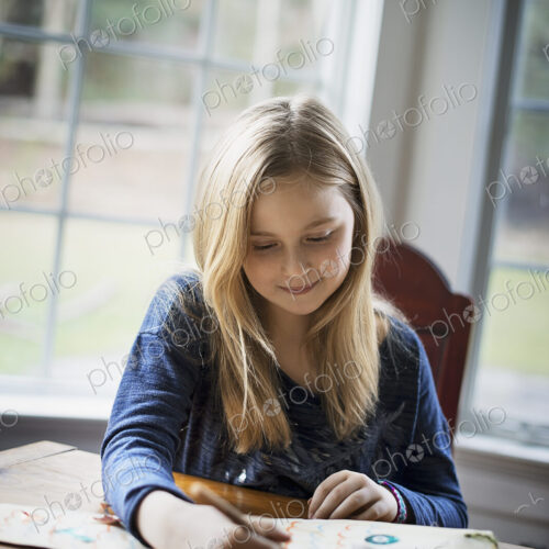 A family home. A young girl sitting at a table drawing on a large piece of paper.…