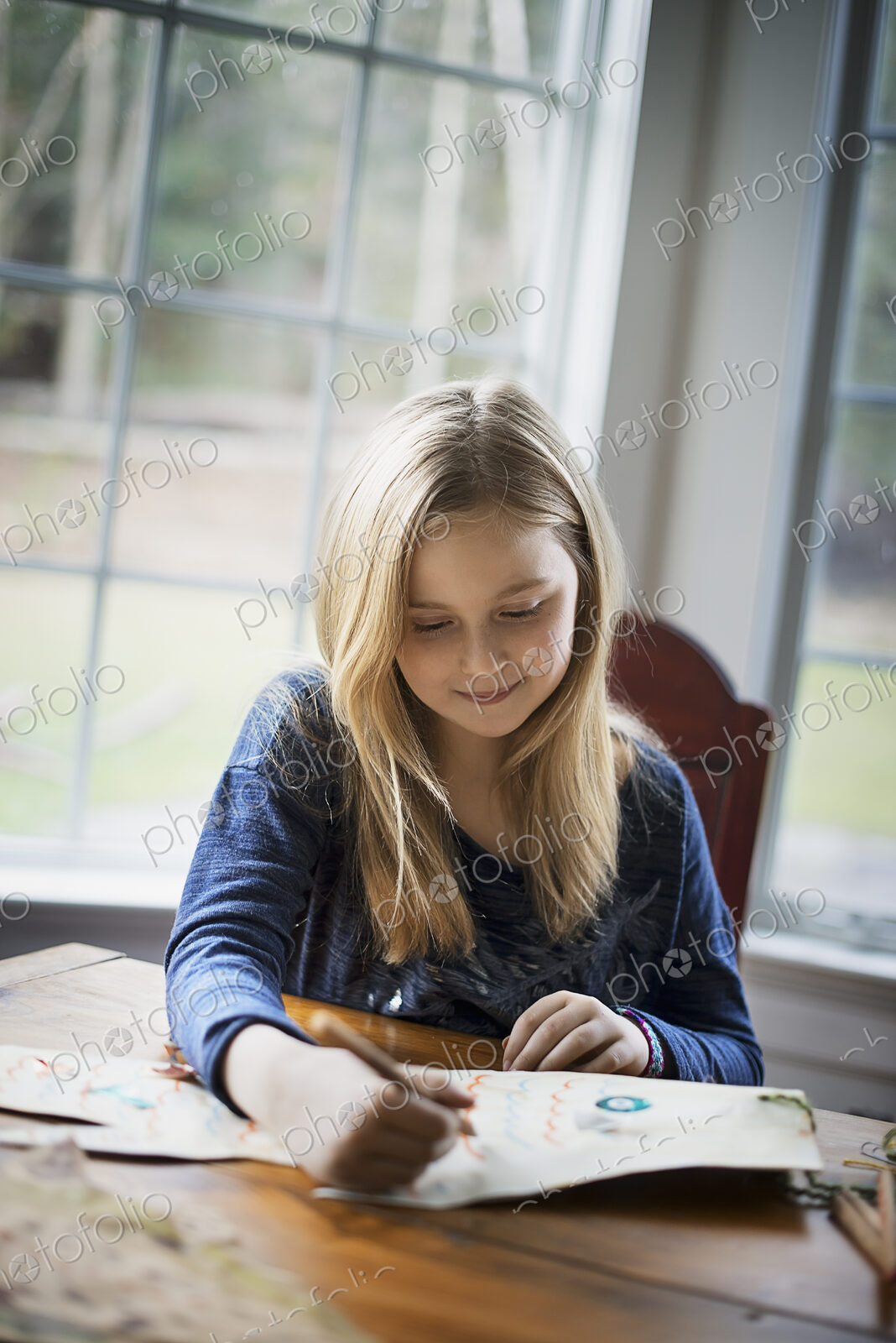 A family home. A young girl sitting at a table drawing on a large piece of paper.…