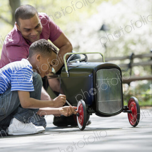 A family in the park on a sunny day. A boy repairing an old fashioned toy peddle car. A family in the park on a sunny day. A boy repairing an old fashioned toy peddle car.
