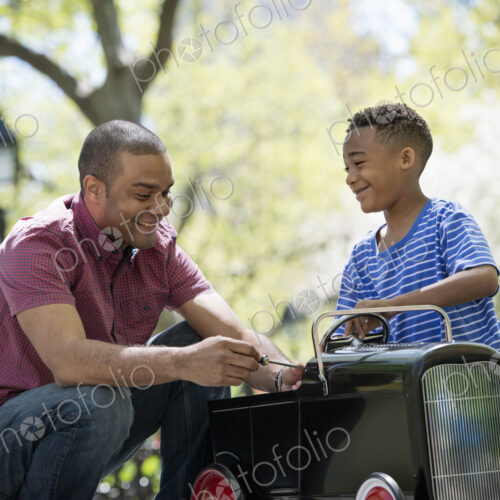 A family in the park on a sunny day. A boy riding an old fashioned toy peddle car. A family in the park on a sunny day. A boy riding an old fashioned toy peddle car.