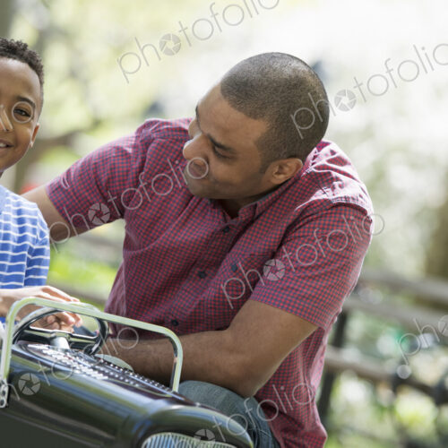 A family in the park on a sunny day. A boy riding an old fashioned toy peddle car. A family in the park on a sunny day. A boy riding an old fashioned toy peddle car.