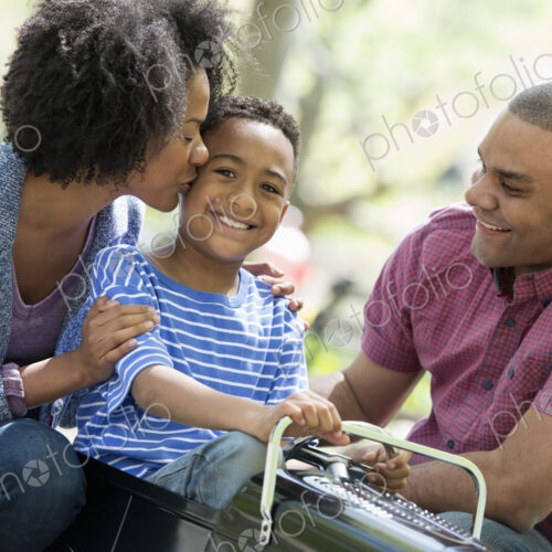 A family in the park on a sunny day. A boy riding an old fashioned toy peddle car. A family in the park on a sunny day. A boy riding an old fashioned toy peddle car.