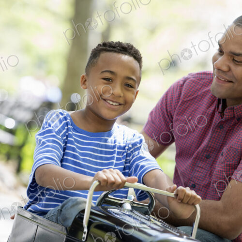 A family in the park on a sunny day. A boy riding an old fashioned toy peddle car. A family in the park on a sunny day. A boy riding an old fashioned toy peddle car.