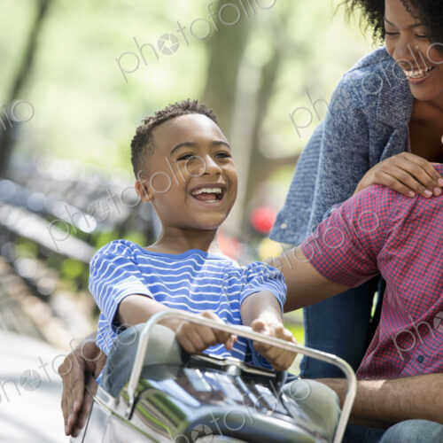 A family in the park on a sunny day. A boy riding an old fashioned toy peddle car. A family in the park on a sunny day. A boy riding an old fashioned toy peddle car.