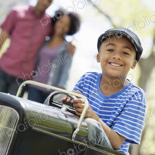 A family in the park on a sunny day. A boy riding an old fashioned toy peddle car. A family in the park on a sunny day. A boy riding an old fashioned toy peddle car.