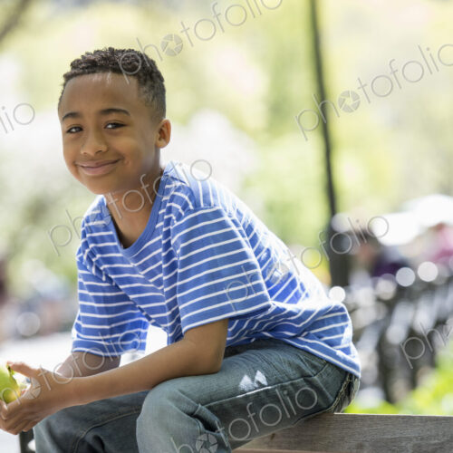 A family in the park on a sunny day. A boy sitting on a fence eating an apple. A family in the park on a sunny day. A boy sitting on a fence eating an apple.