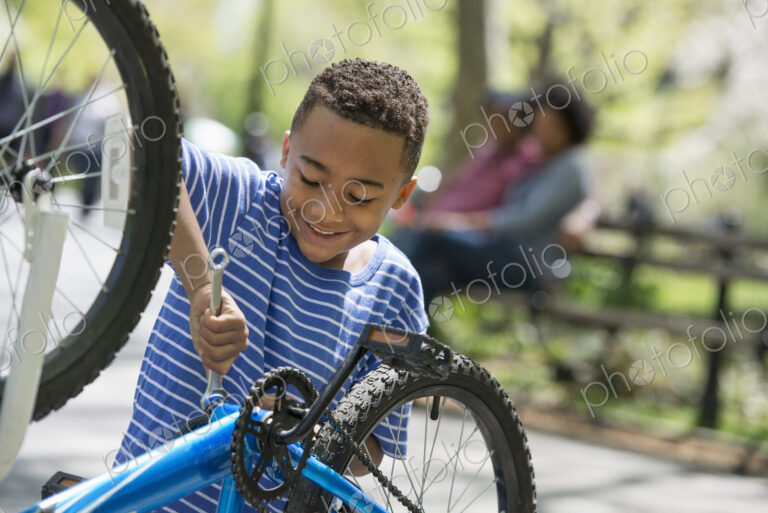 A family in the park on a sunny day. A father and son repairing a bicycle.