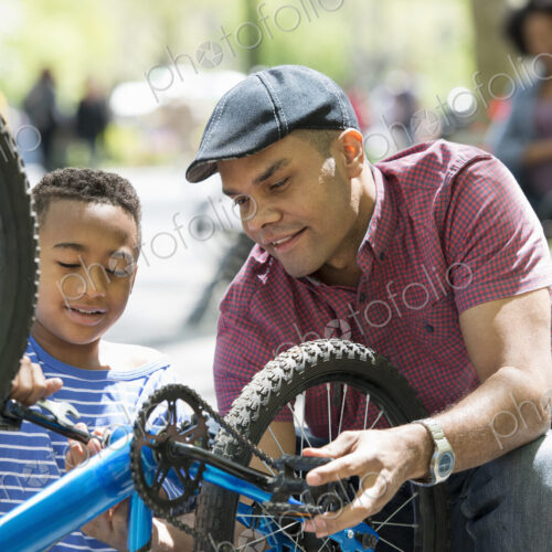 A family in the park on a sunny day. A father and son repairing a bicycle. A family in the park on a sunny day. A father and son repairing a bicycle.
