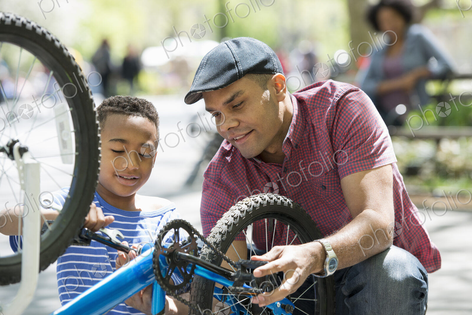 A family in the park on a sunny day. A father and son repairing a bicycle.
