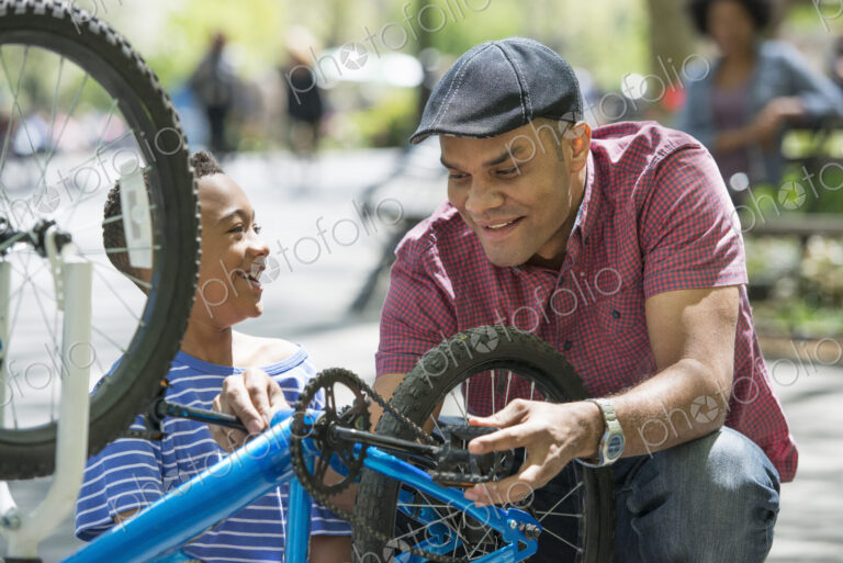 A family in the park on a sunny day. A father and son repairing a bicycle.
