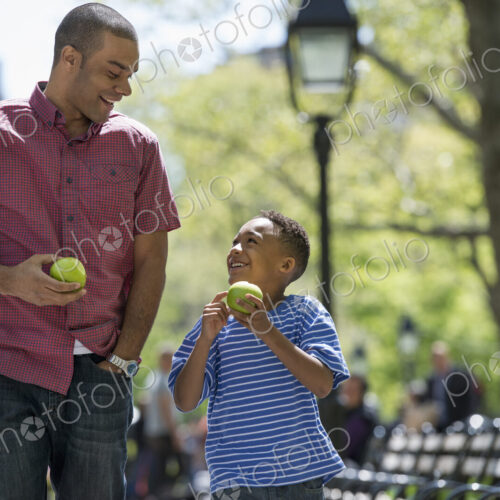 A family in the park on a sunny day. A man and a boy eating apples. A family in the park on a sunny day. A man and a boy eating apples.