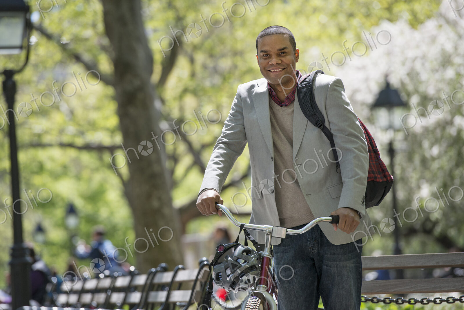 A family in the park on a sunny day. A man pushing a bicycle.