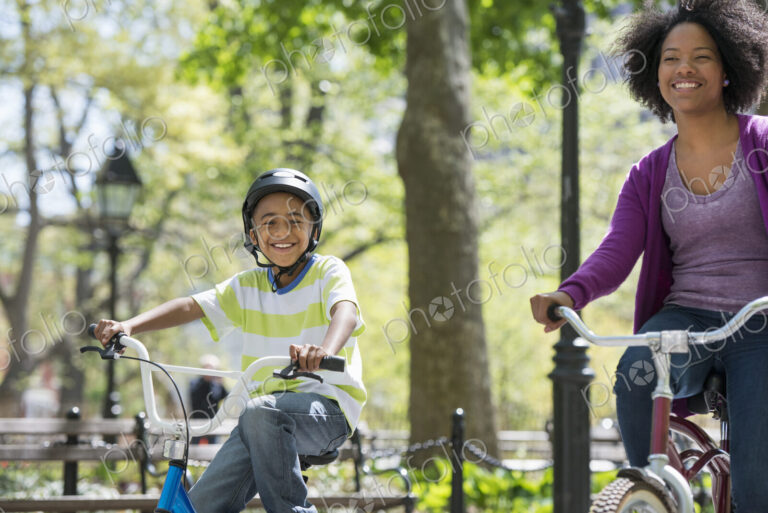 A family in the park on a sunny day. A mother and son cycling on a path.