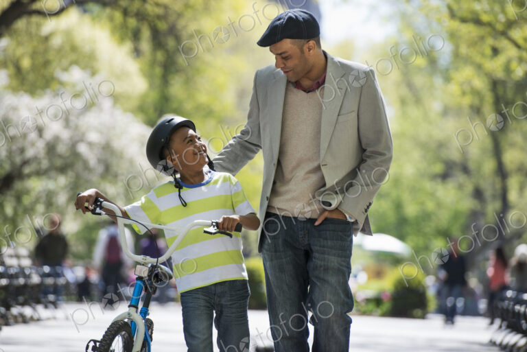 A family in the park on a sunny day. Bicycling and having fun. A father and son side…
