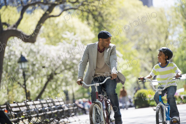 A family in the park on a sunny day. Bicycling and having fun. A father and son side…