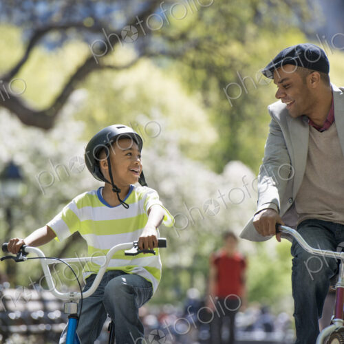 A family in the park on a sunny day. Bicycling and having fun. A father and son side…