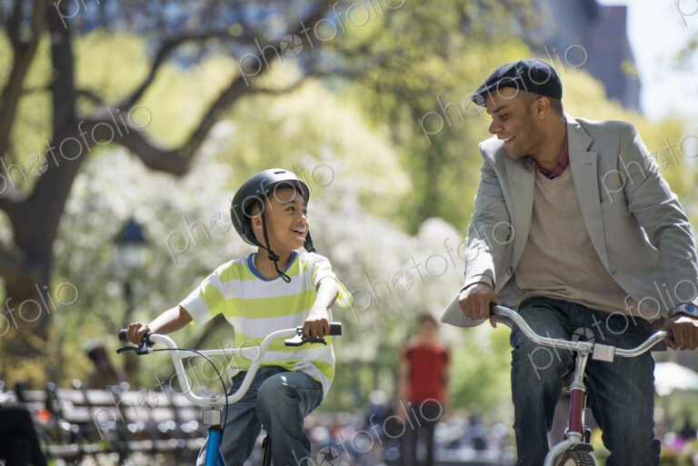 A family in the park on a sunny day. Bicycling and having fun. A father and son side…