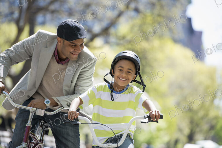 A family in the park on a sunny day. Bicycling and having fun. A father and son side…