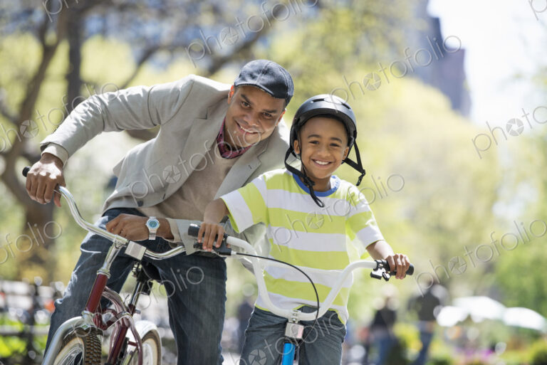 A family in the park on a sunny day. Bicycling and having fun. A father and son side…