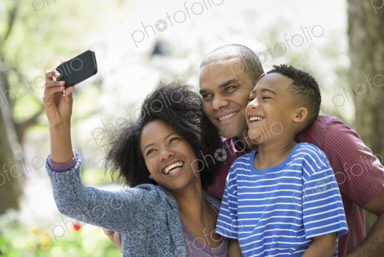 A family in the park on a sunny day. Two adults and a young boy taking photographs…
