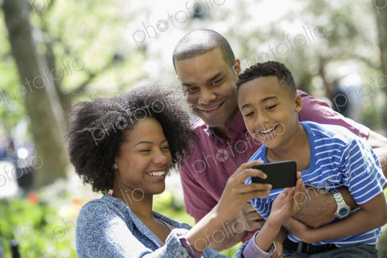 A family in the park on a sunny day. Two adults and a young boy taking photographs…