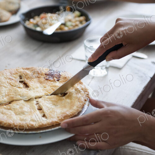 A family meal. A person cutting a pie with a knife.