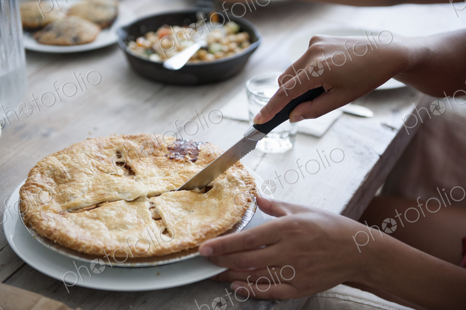 A family meal. A person cutting a pie with a knife.
