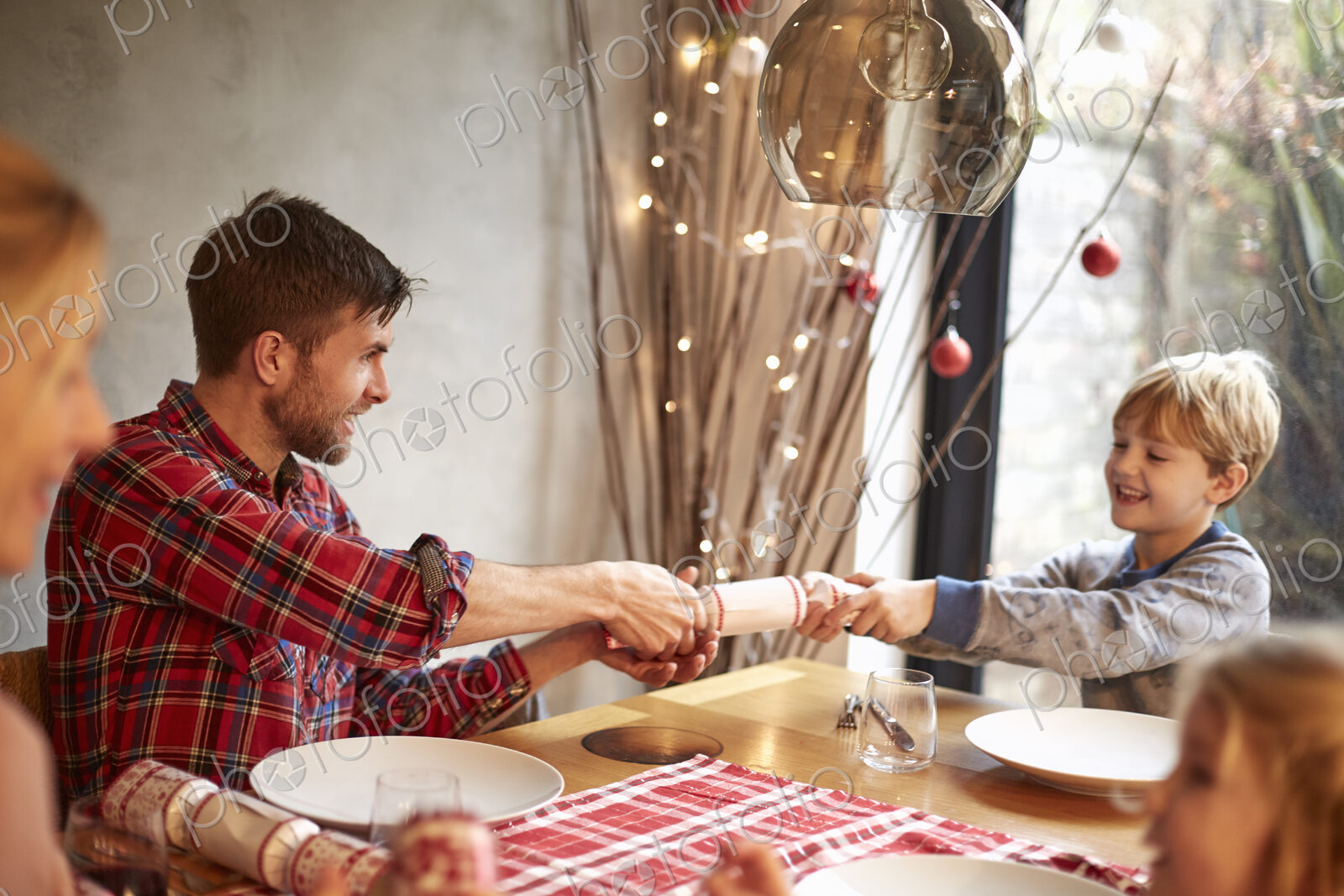 A family of four people at a table at Christmas, pulling crackers.