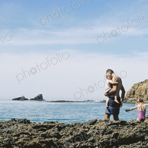 A family on holiday, two adults with their son and daughter walking across rocks by… A family on holiday, two adults with their son and daughter walking across rocks by…