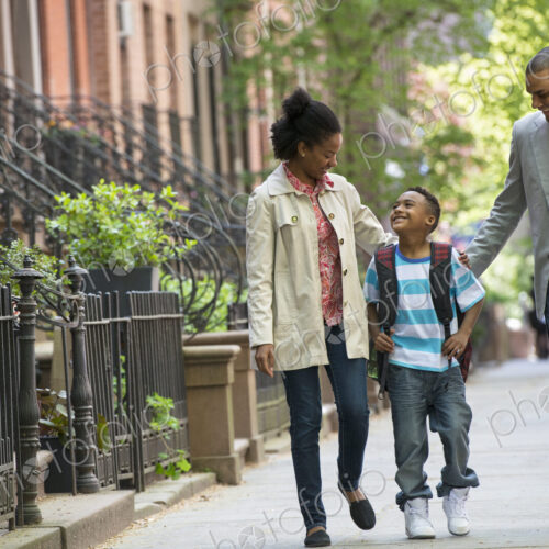 A family outdoors in the city. Two parents and a young boy walking together.