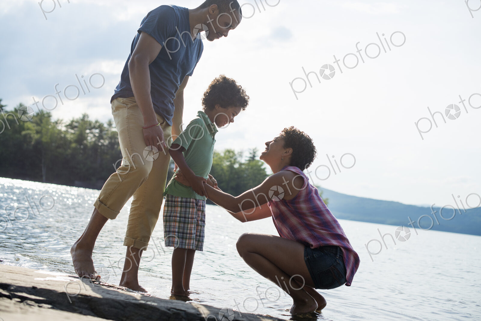 A family, parents and son spending time together by a lake in summer.