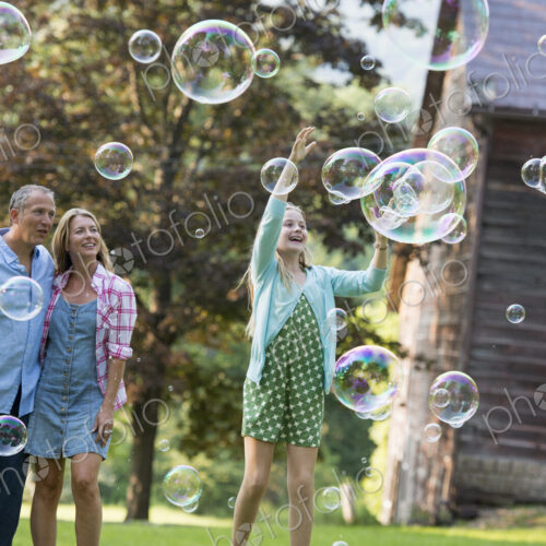 A family sitting on the grass outside a bar, blowing bubbles and laughing.